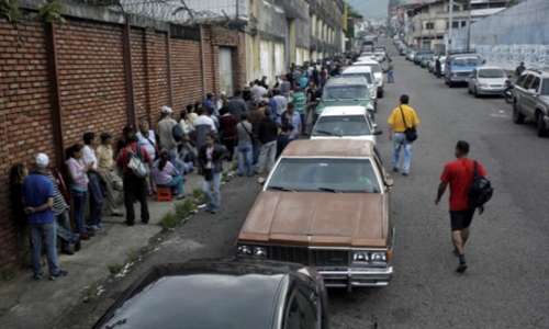 Dòng người xếp hàng trước cửa siêu thị cạnh dãy ôtô chờ mua xăng tại San Cristobal. Ảnh: Reuters